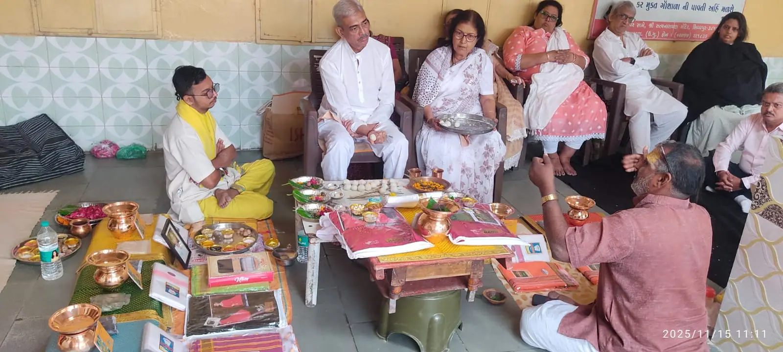 A purohit explaining the rite to a family seated in a ritual hall, with copper kalash and offerings arranged before them