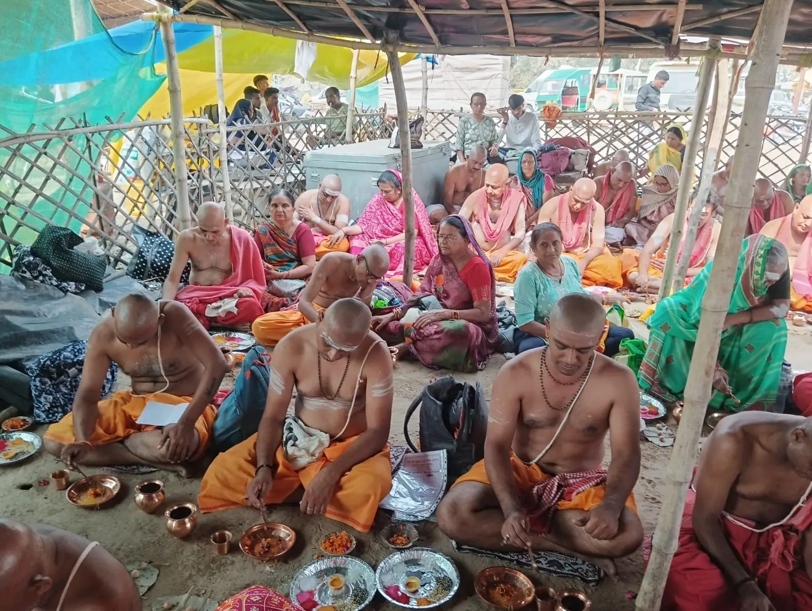 Families seated under a temporary shade with copper vessels and offerings during a busy day of Matrugaya rites
