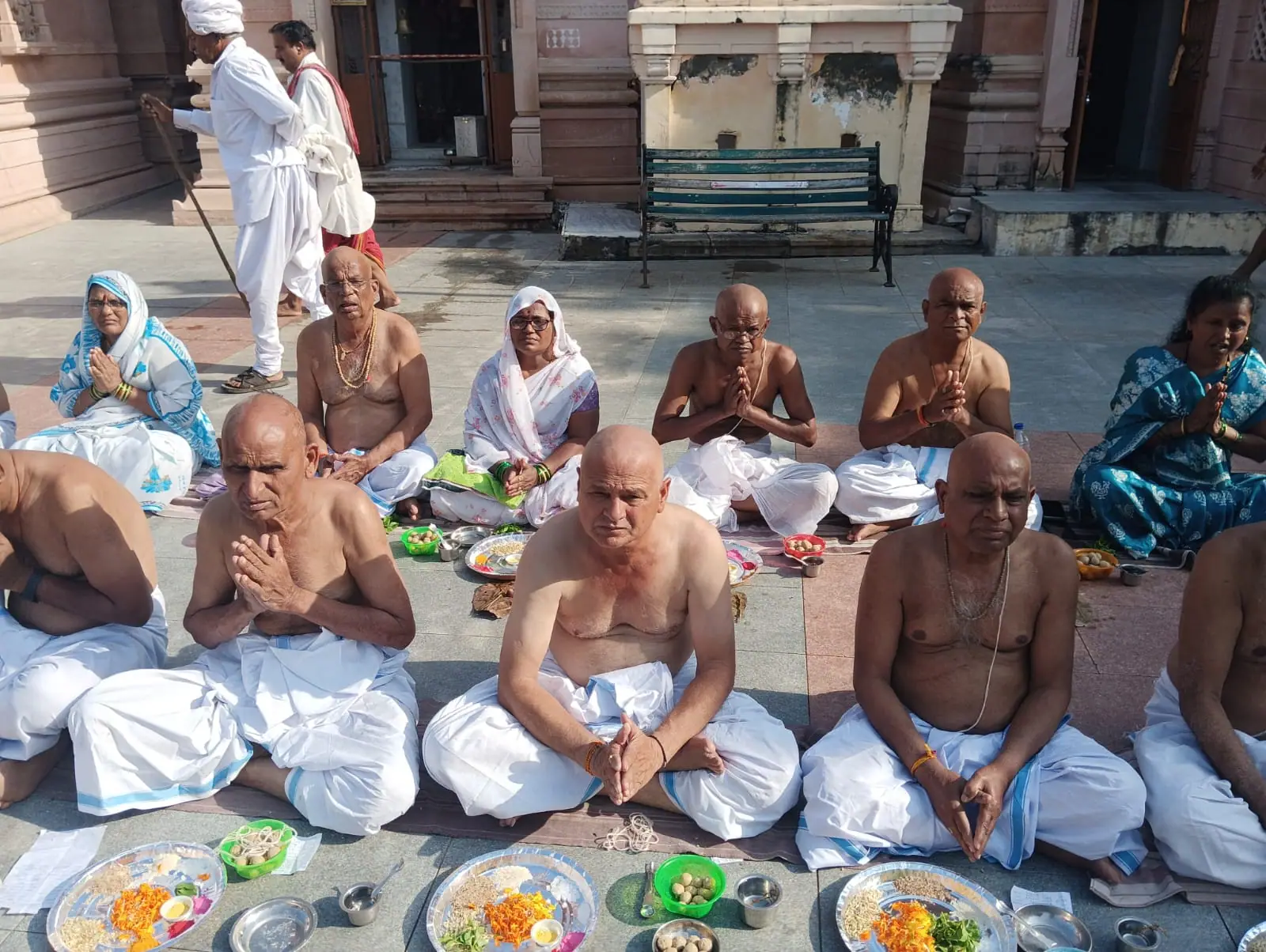 Men in white dhotis with folded hands seated before leaf plates of offerings in the Bindu Sarovar complex