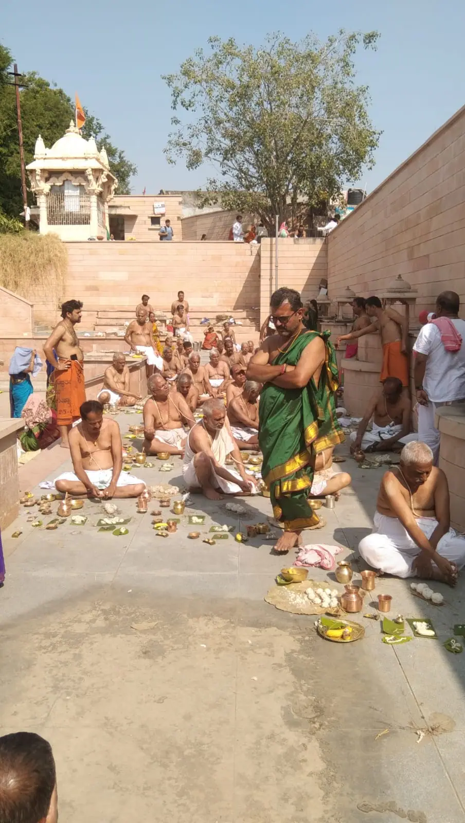 Pilgrims performing rites on the stone floor of the Bindu Sarovar tank, with steps and a white shrine behind